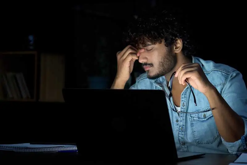 Man in a dark room working late in front of his laptop