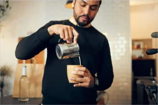 Man pouring milk into his freshly brewed cappuccino