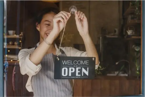 Owner hanging open sign in the window of her small business